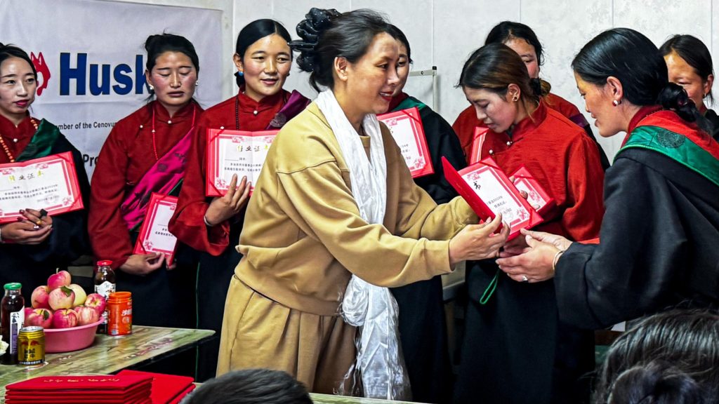 A group of women in red and black attire distributes certificates to attendees at an event.