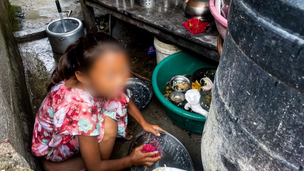 A little girl washes dishes in a small outdoor kitchen.
