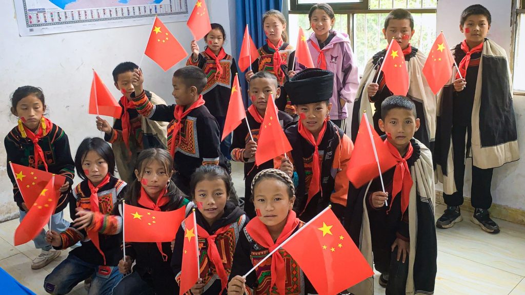 A group of children joyfully holding Chinese flags, smiling and standing together.