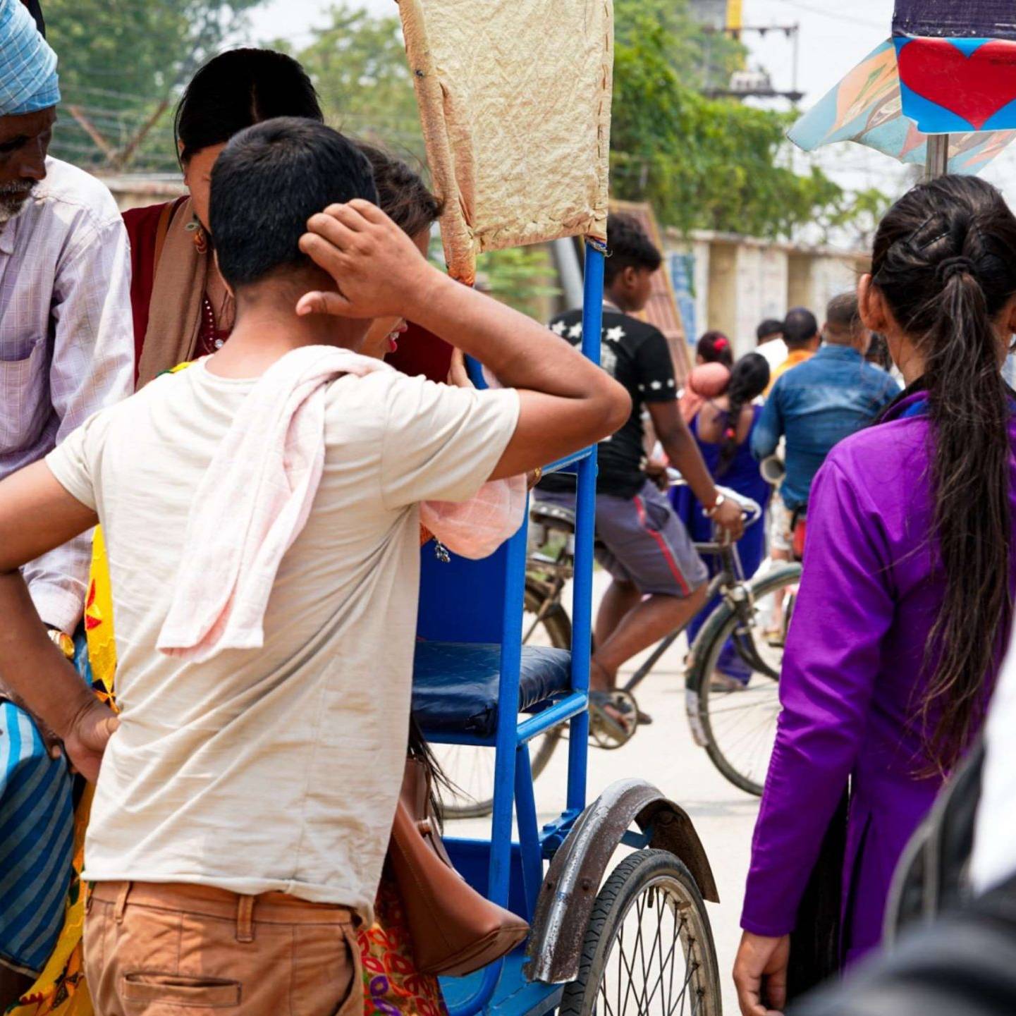 A man and a woman standing by the road next to a man riding a rickshaw with a female passenger.