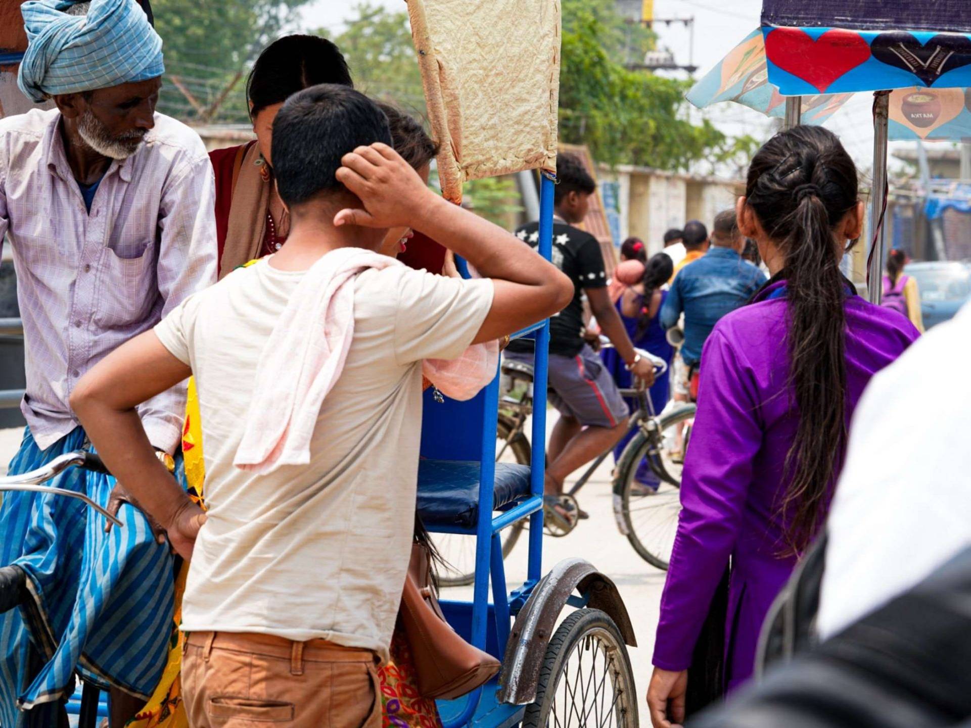 A man and a woman standing by the road next to a man riding a rickshaw with a female passenger.