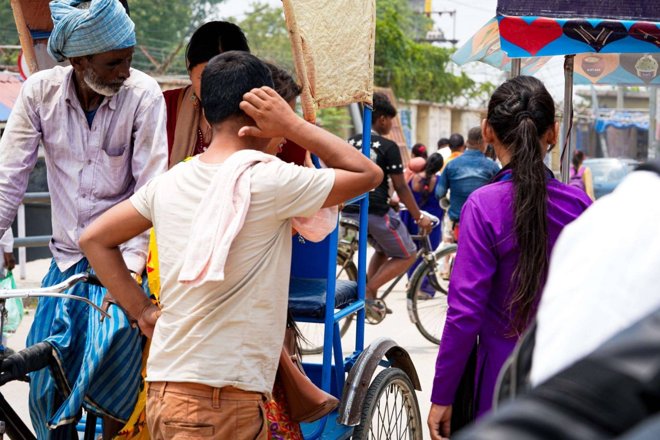 A man and a woman standing by the road next to a man riding a rickshaw with a female passenger.