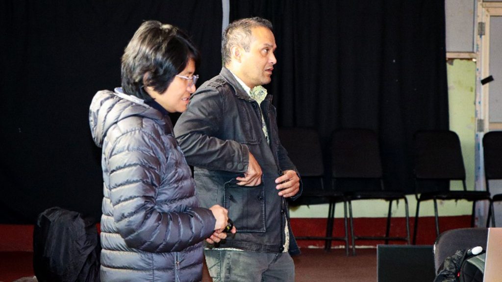 A man and a woman standing side by side in front of a laptop, appearing to be giving a presentation.
