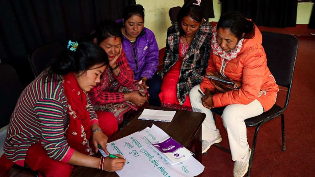 Women seated around a table engaged in a discussion while one of them writes their ideas down.