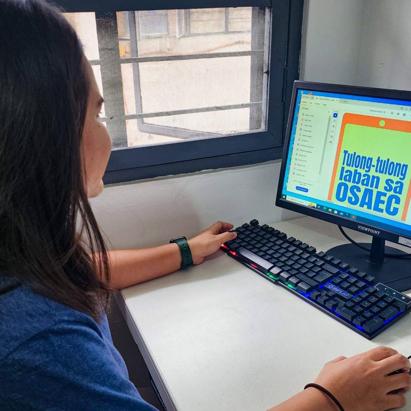 A woman focused on her computer, creating a design with graphic software in a well-lit workspace.