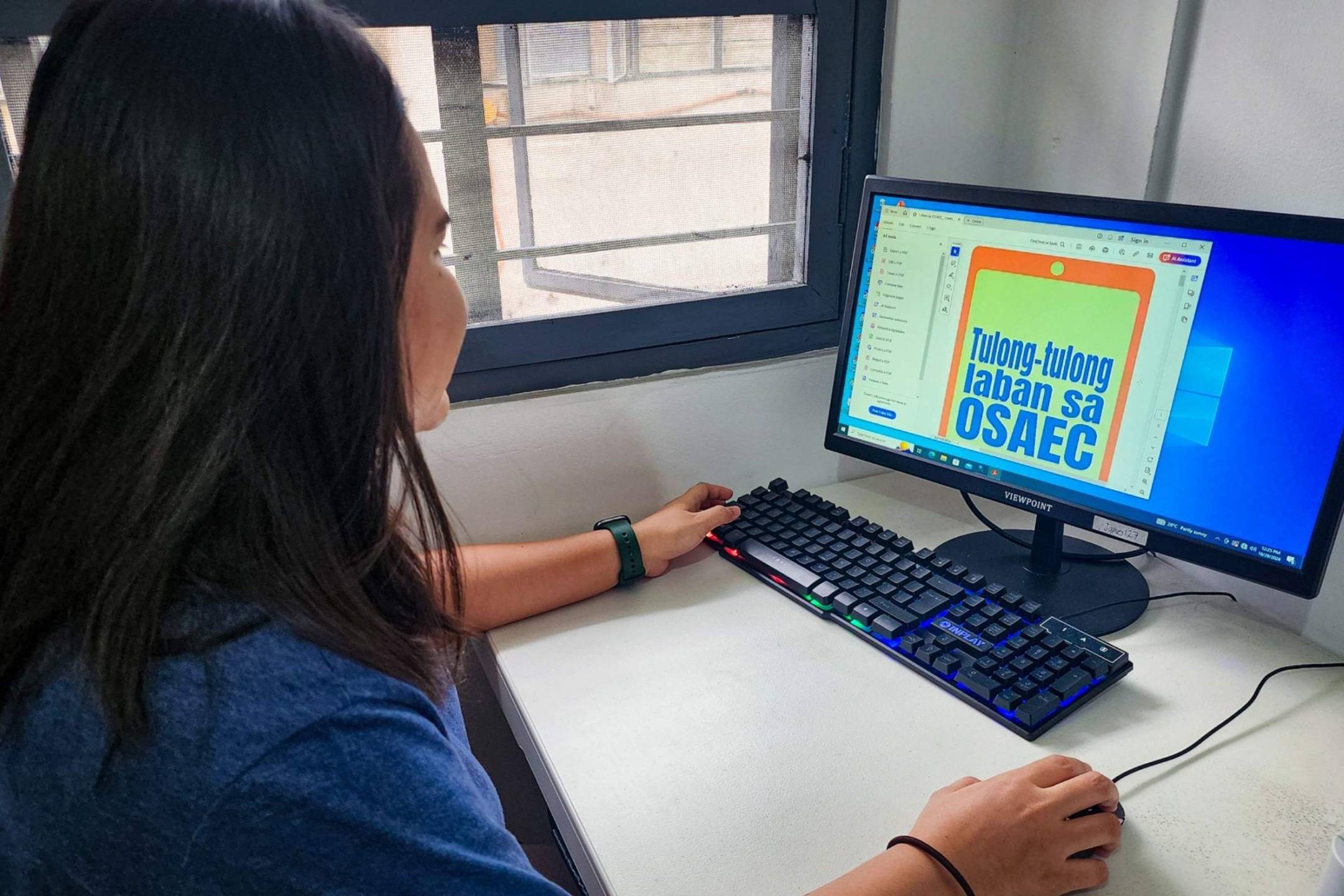 A woman focused on her computer, creating a design with graphic software in a well-lit workspace.