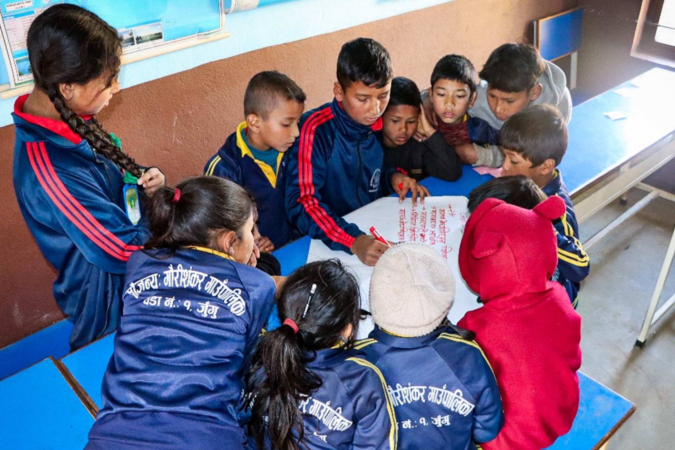Several children in a classroom focused on a paper, engaged in discussion.