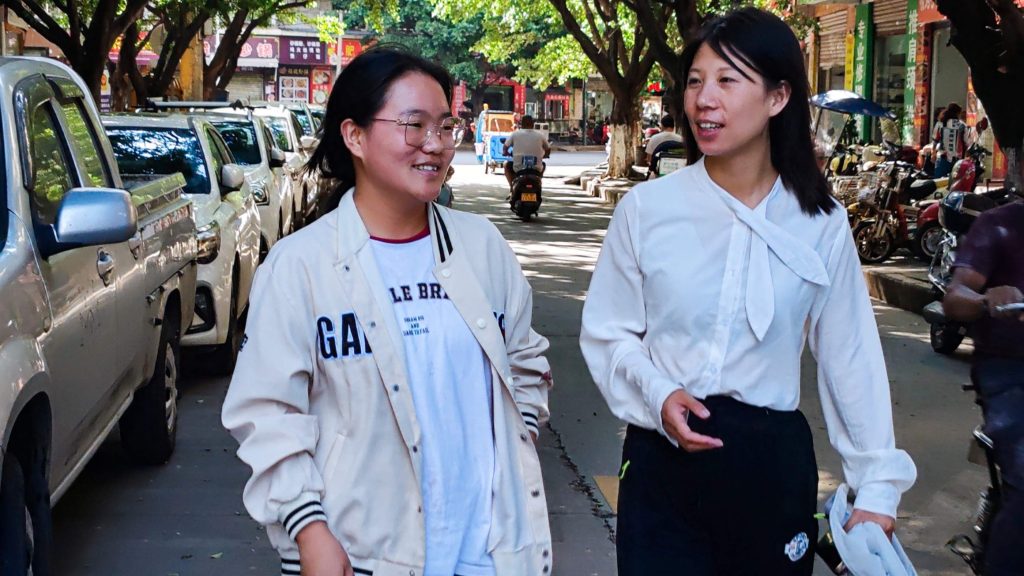 Two women walking side by side down a bustling city street, surrounded by buildings and urban scenery.