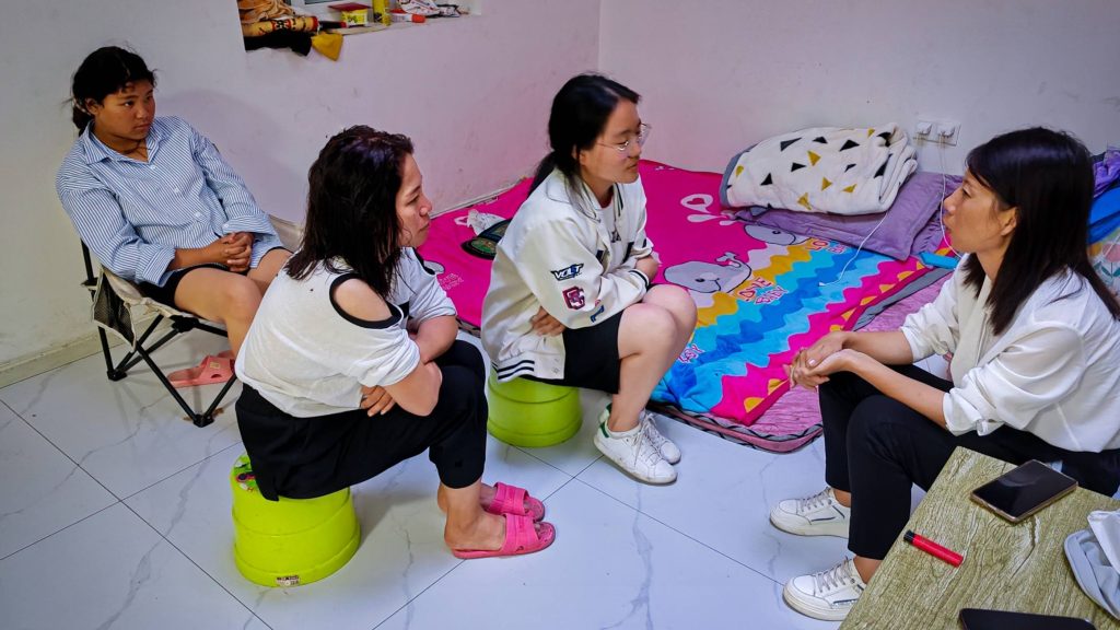 Four women sitting on the floor in a cozy room, engaged in conversation and sharing smiles.