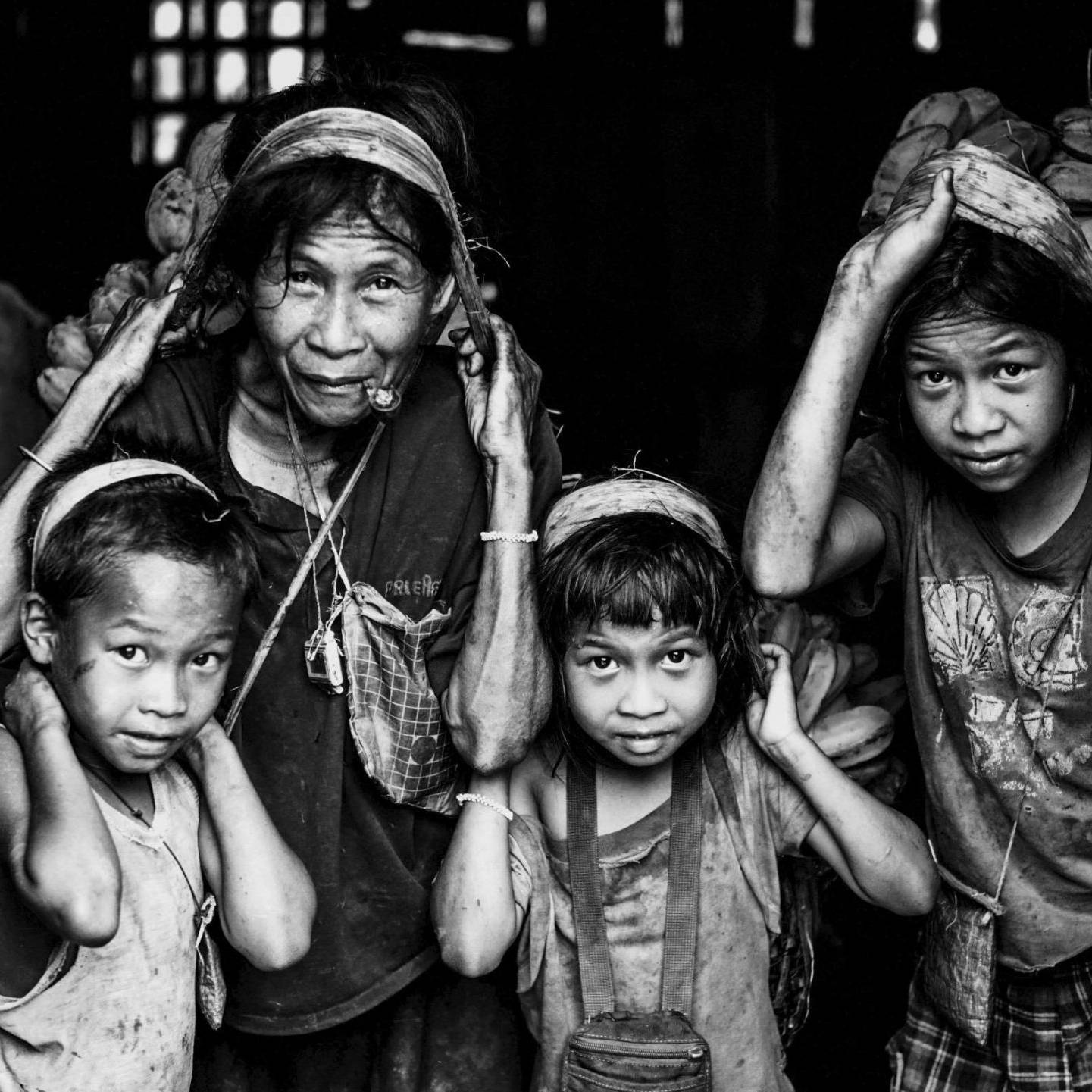 Several children are gathered in a barn, carrying bunches of bananas.