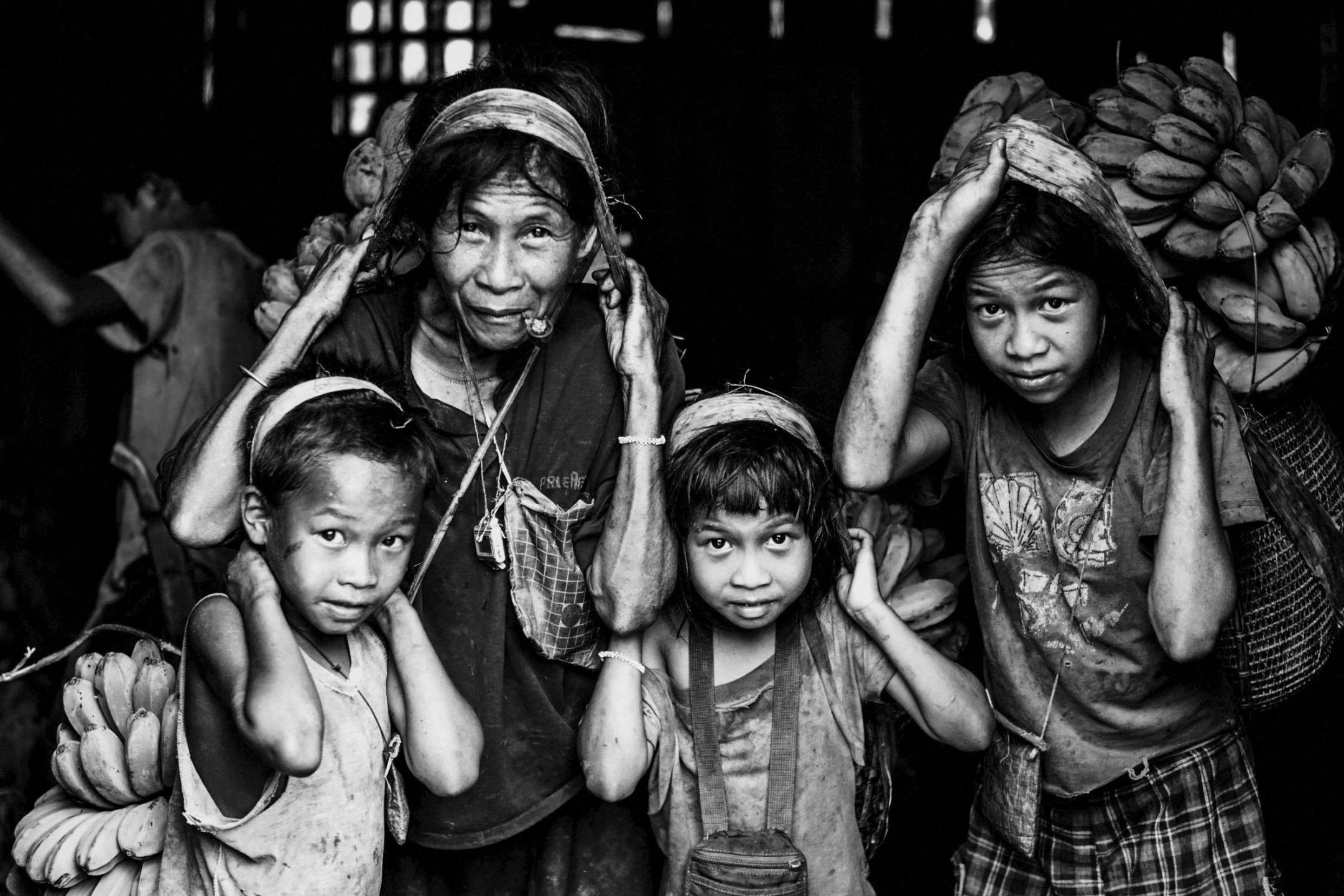 Several children are gathered in a barn, carrying bunches of bananas.
