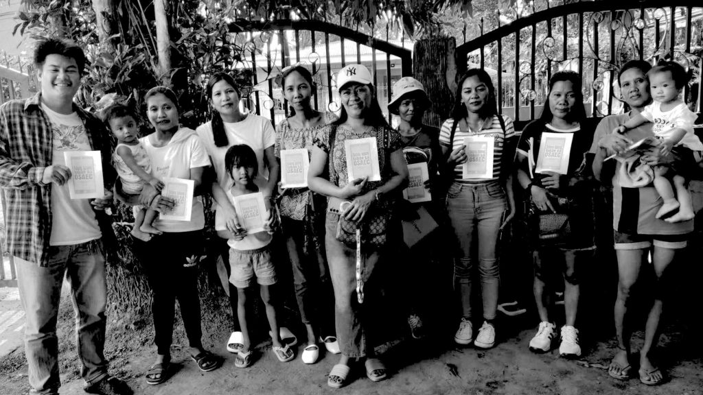A group of people stands in front of a gate, holding papers and discussing among themselves.