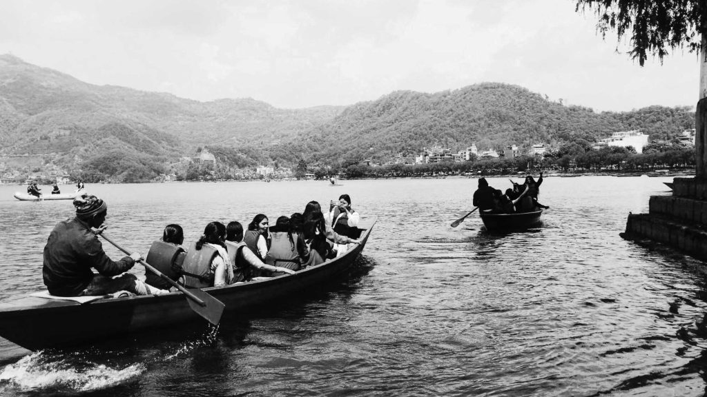 A group of people paddling together in a canoe on a calm body of water surrounded by greenery.