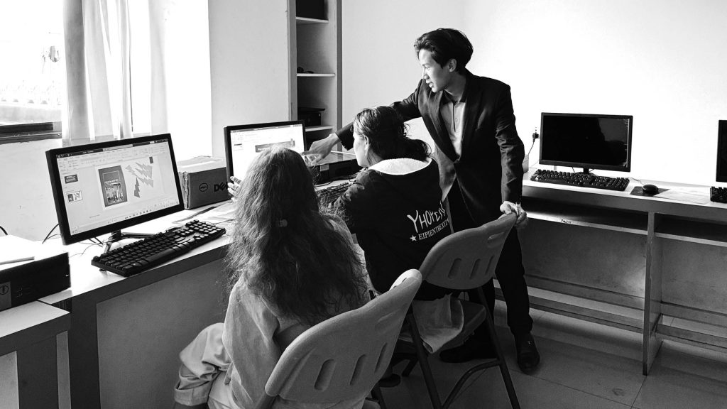 A man and two women collaborate on computers in a classroom setting, focused on their tasks.