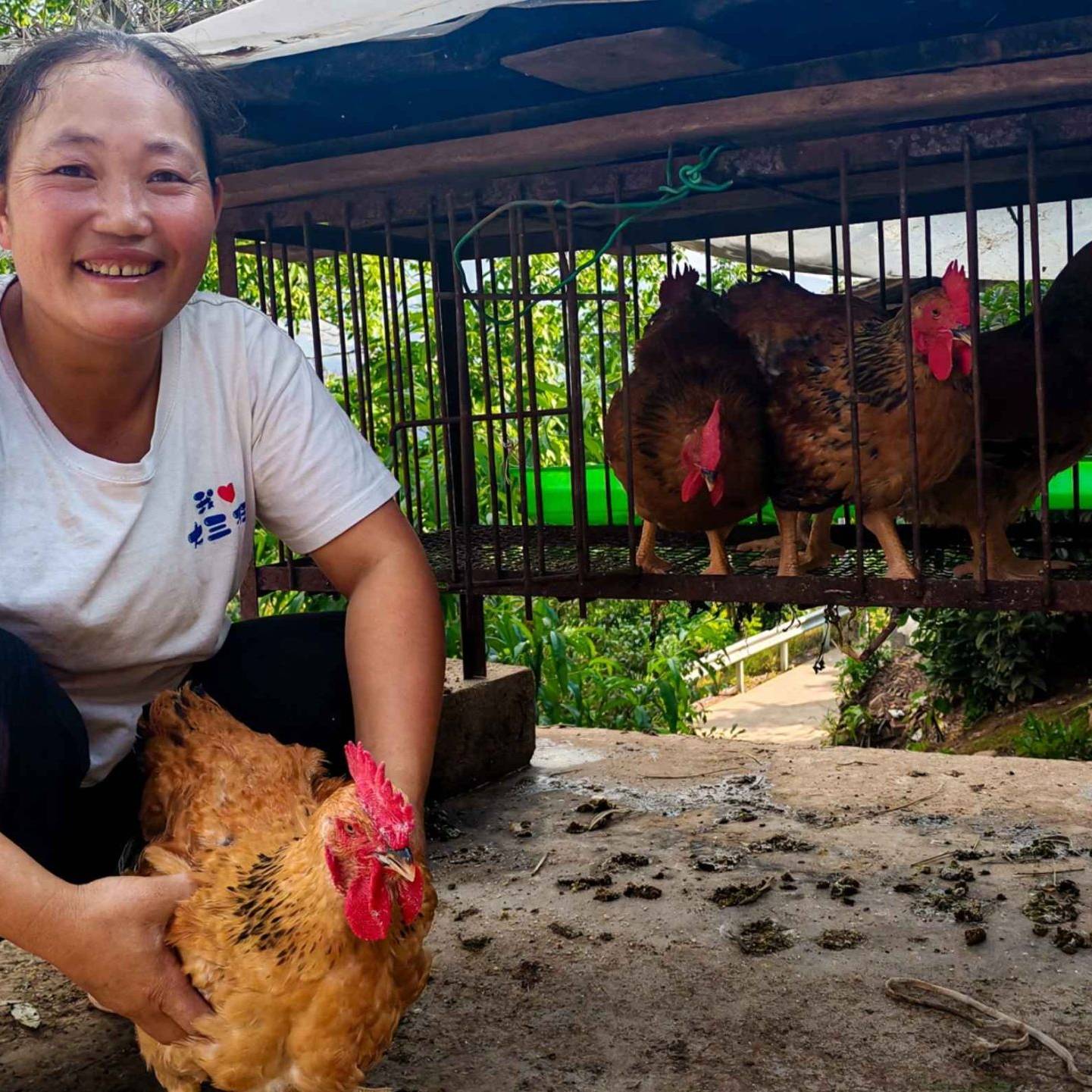 A woman holds a chicken in front of a cage.
