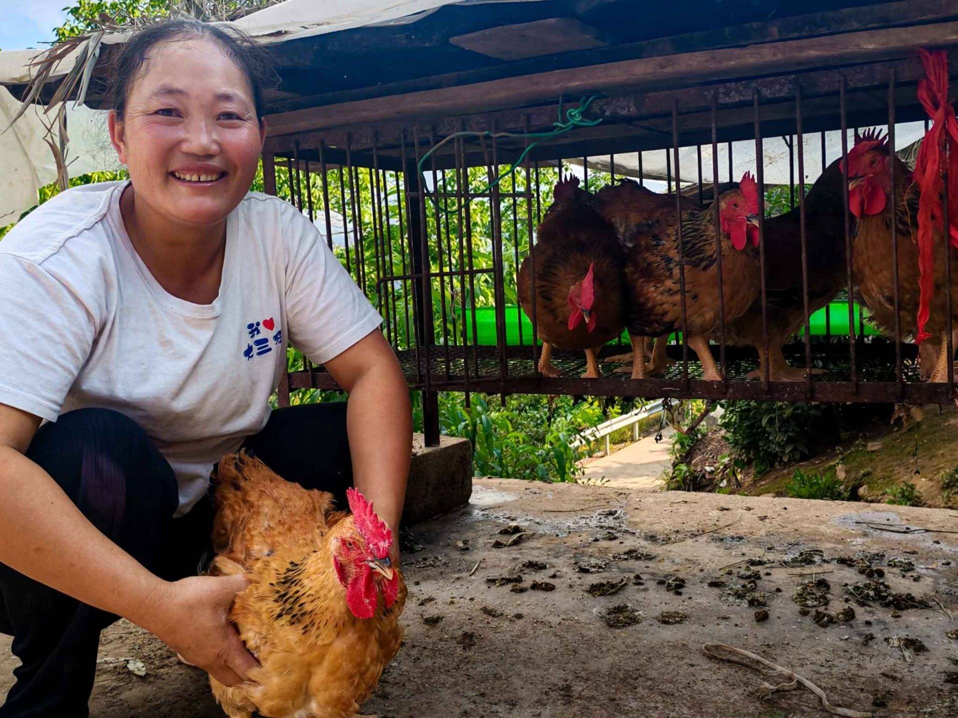 A woman holds a chicken in front of a cage.