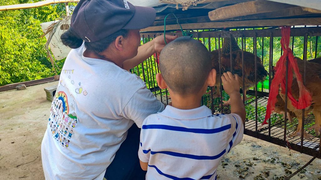 A woman and a child gently pet chickens inside a cage.