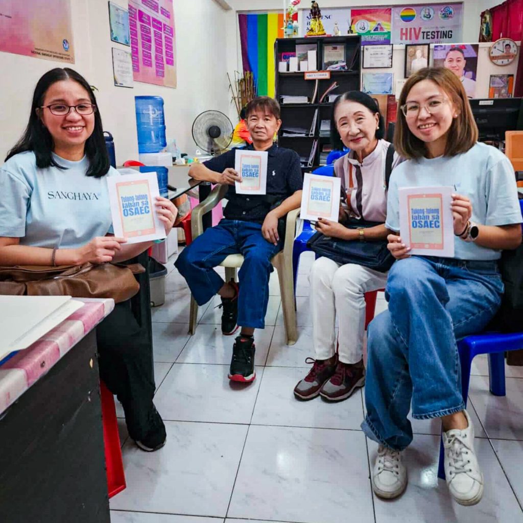 Four individuals seated in chairs, each holding a book and smiling at the camera.