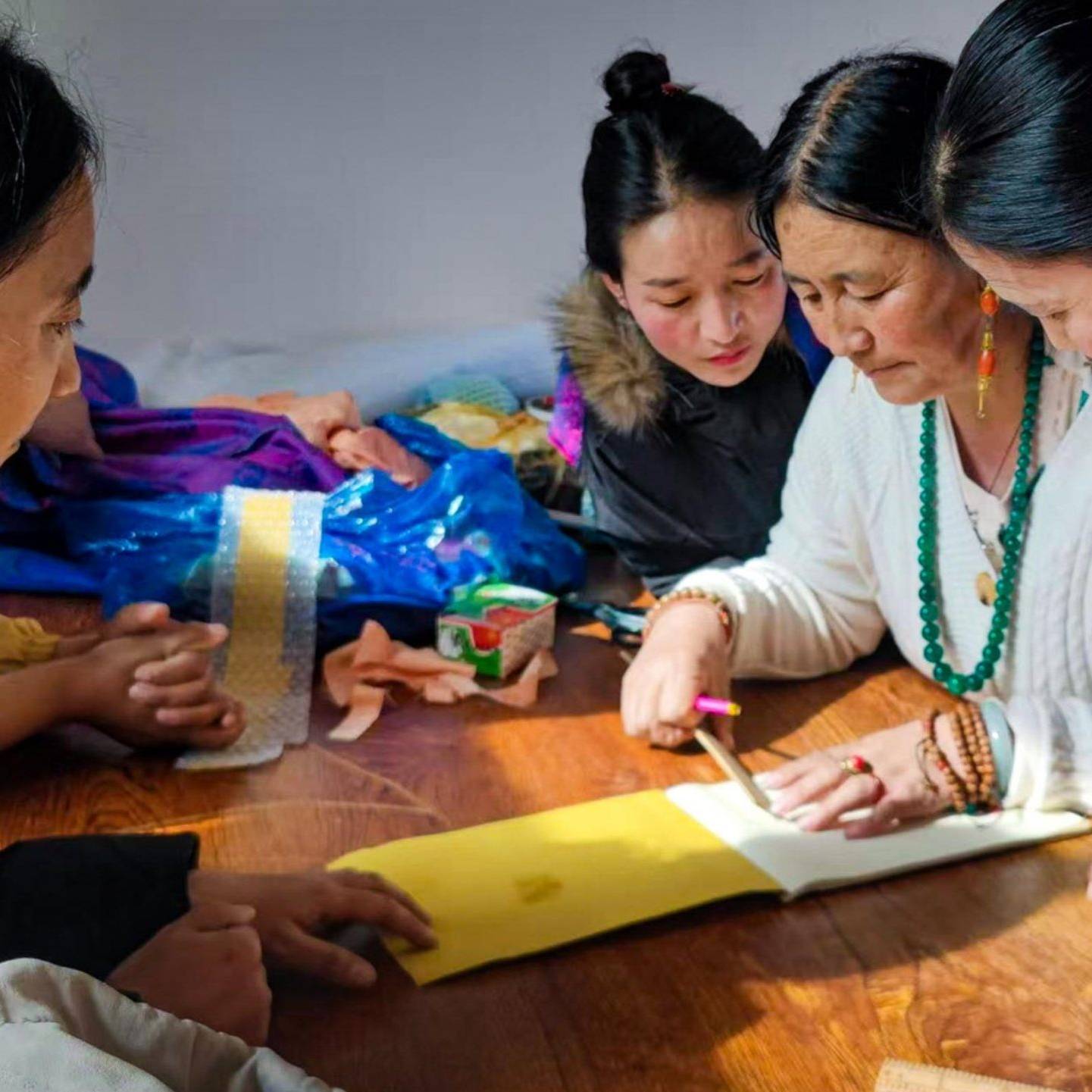 A group of four women gathers closely around a table, focused on crafting with bright materials. Their expressions show concentration and collaboration.