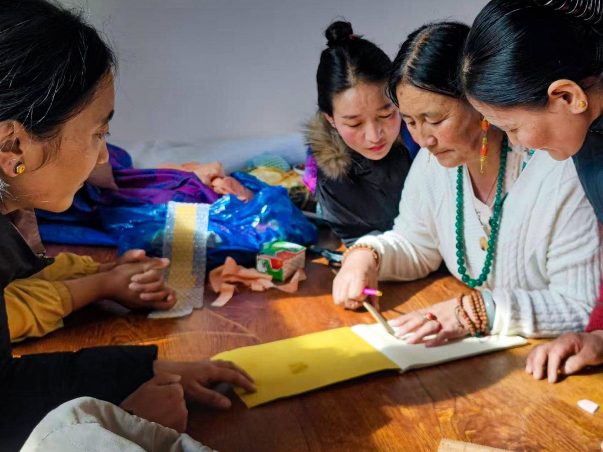 A group of four women gathers closely around a table, focused on crafting with bright materials. Their expressions show concentration and collaboration.