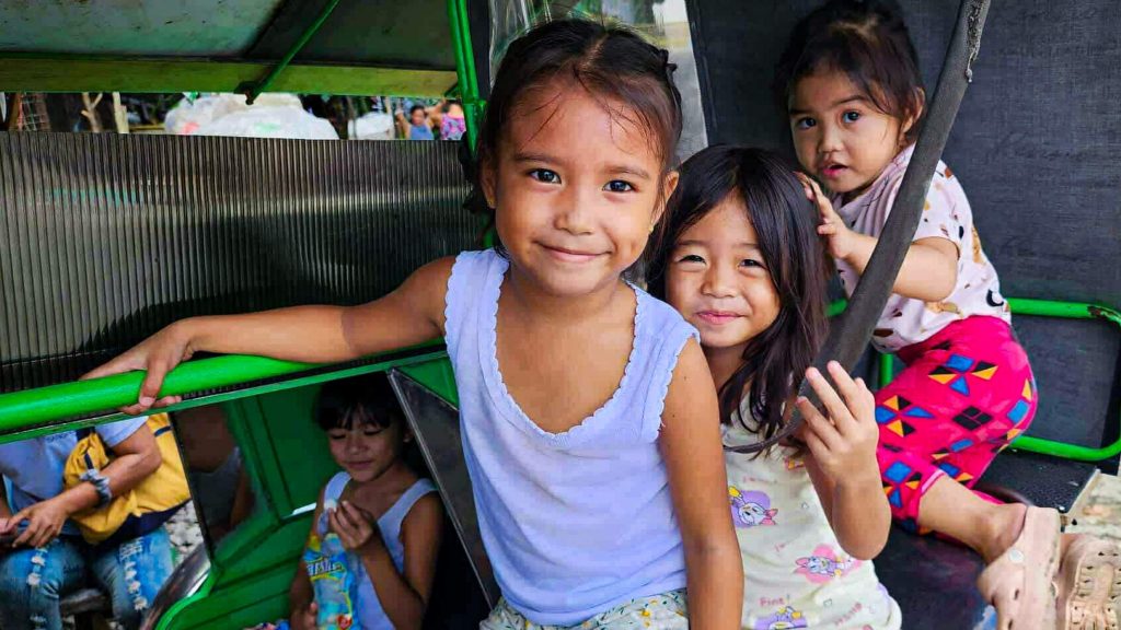 Three smiling young girls sit in a colorful tricycle, exuding joy and playfulness.