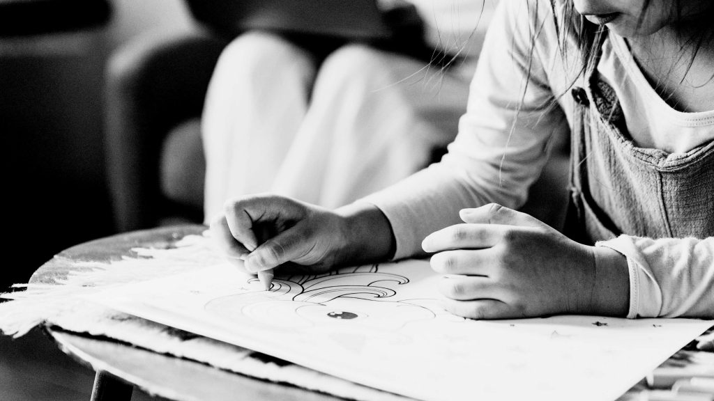 A child engaged in coloring a drawing on a table, concentrating intently. Black and white image conveys a calm, creative atmosphere.