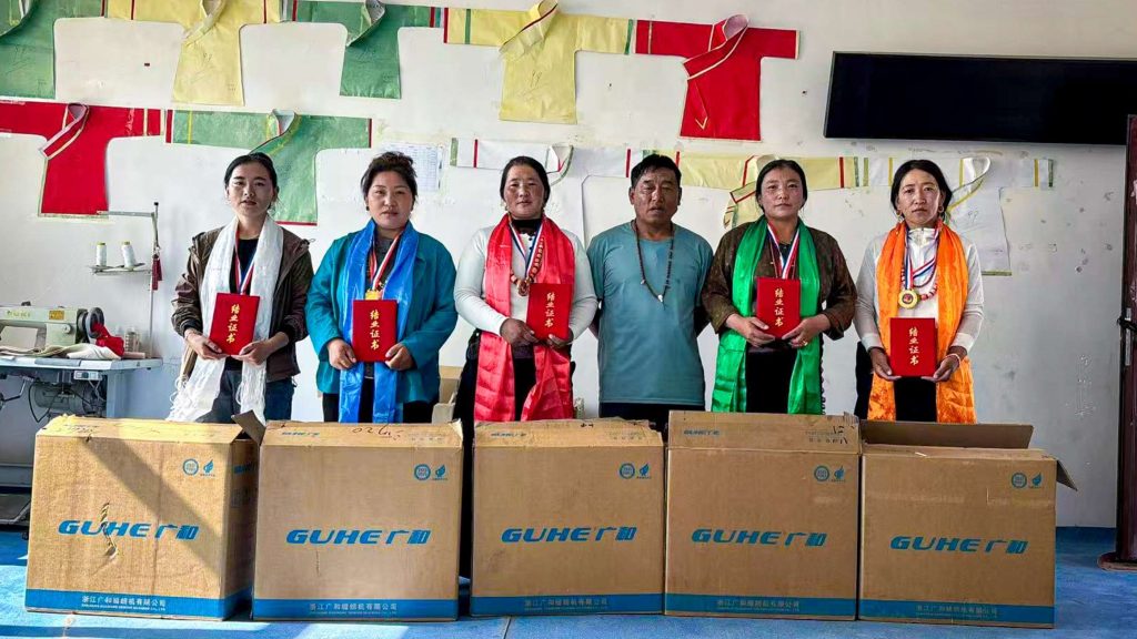 Six people stand in a line, each holding a red certificate and wearing medals. They are in front of large boxes. The mood is celebratory.