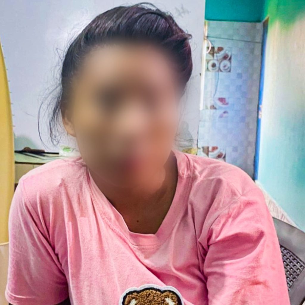 A person in a pink T-shirt with a bear design stands indoors with a blurred face for privacy, conveying a casual and relaxed mood. The room is softly lit.