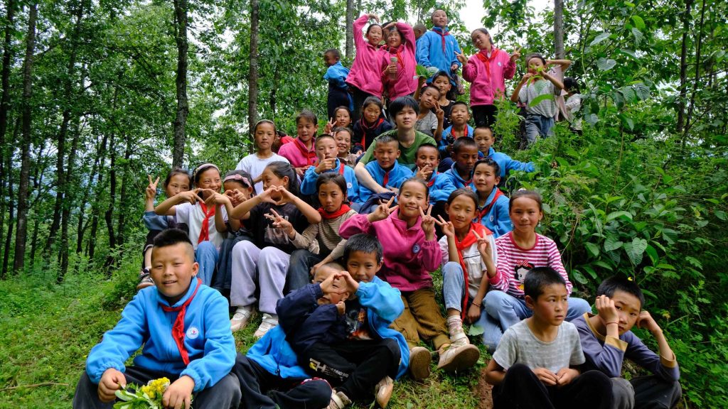 A group of children in colorful clothing pose playfully in a lush forest. The scene conveys joy and camaraderie among the vibrant greenery.