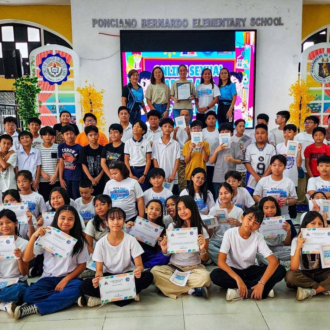A group of students at Ponciiano Bernardo Elementary School proudly display certificates in a colorful auditorium, smiling and celebrating their achievements.
