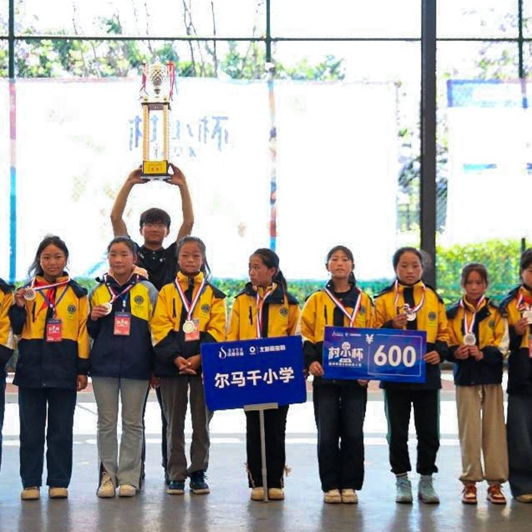 A group of young students in yellow jackets stand together indoors, celebrating a victory. They hold medals and trophies, smiling proudly.