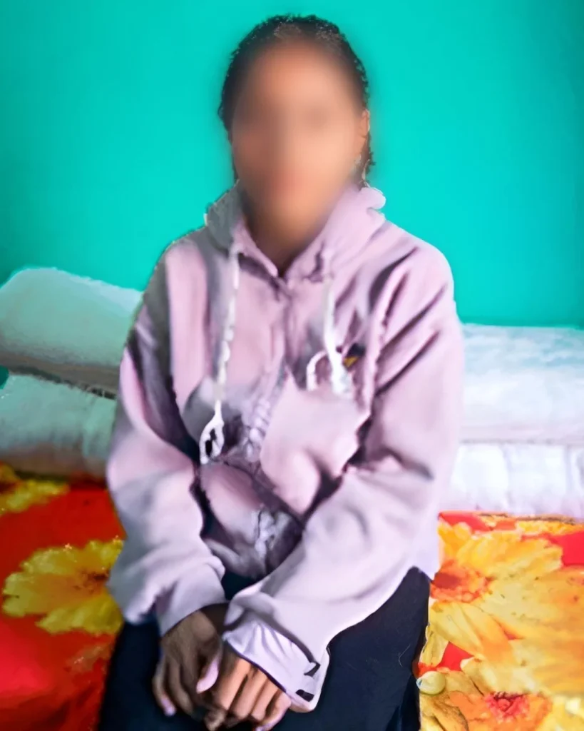 A person in a purple hoodie sits on a colorful floral bedspread against a turquoise wall, conveying a relaxed, calm atmosphere. Her face blurred for privacy.