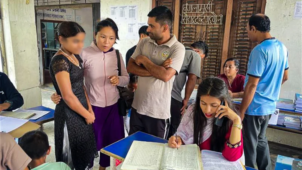 A busy scene shows people standing around tables with documents. A woman is on the phone, highlighting an atmosphere of focused activity.