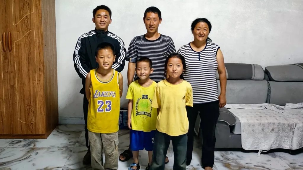 A family of four poses with a staff member in a rural Chinese living room, showcasing their home environment.
