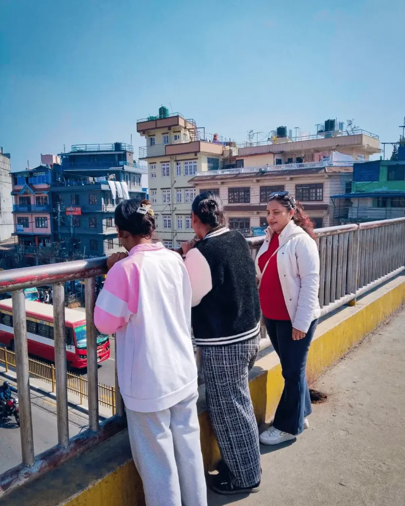 Three women stand and talk together on a bridge