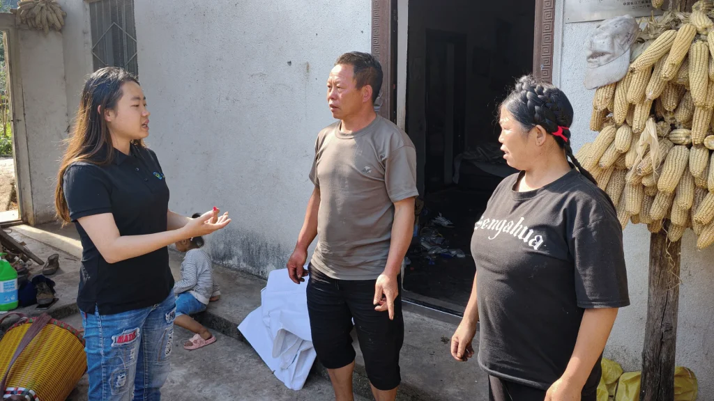 Three adults stand outside in conversation, with corn cobs hanging nearby.