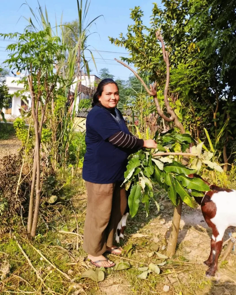 A woman holds a small green plant in her hand, smiling as she admires it.