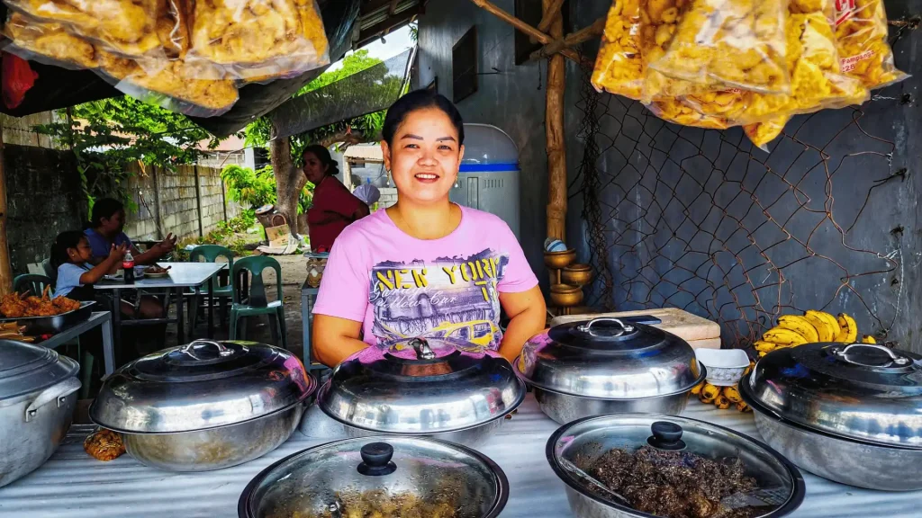 A woman sells homemade food at a vibrant market, engaging with customers and showcasing her tasty offerings.