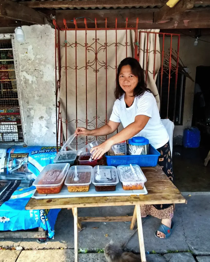 A woman poses in front of a table laden with an array of ingredients to make halo-halo.