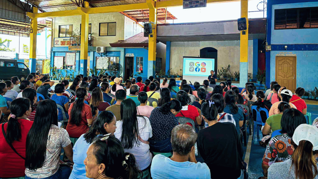 A packed audience in a building, all eyes on the large screen.