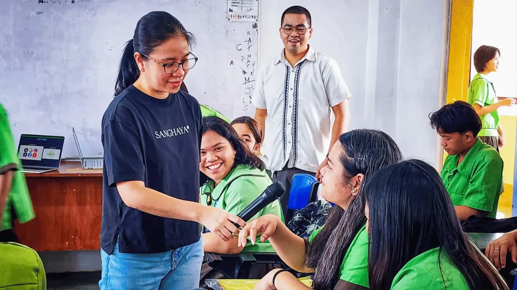 A woman in a green shirt and black pants is engaged in a conversation with students, promoting interaction and connection.
