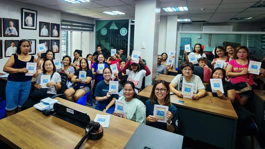 A group of women in a classroom proudly holding up their booklets.