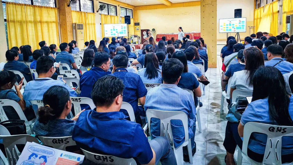 A large group of people seated in chairs, attentively watching a presentation on a screen in front of them.