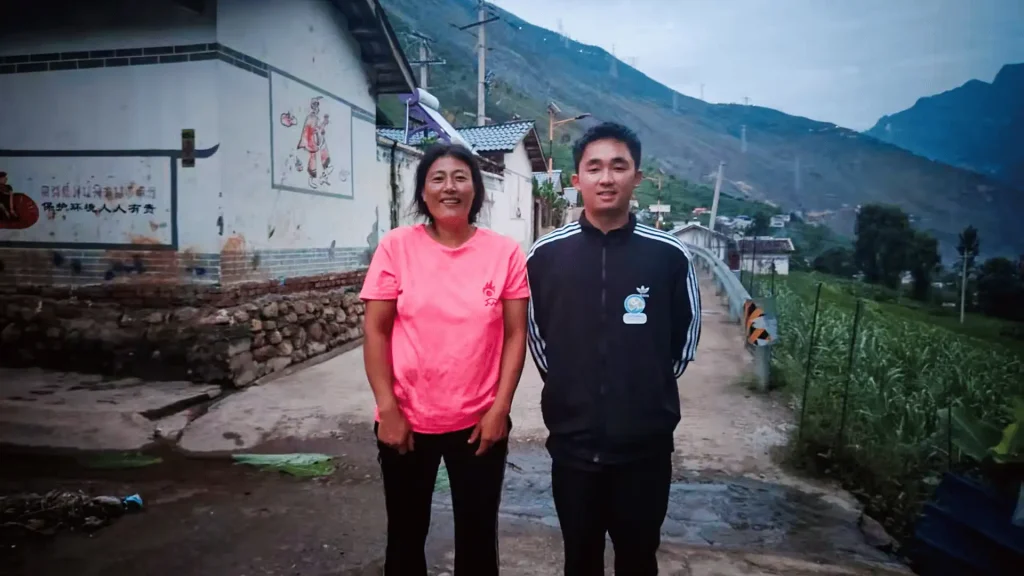 Two individuals stand side by side in front of a house, appearing friendly and engaged.