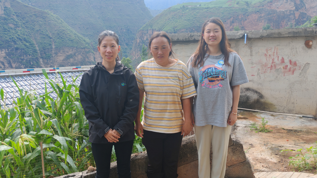 Three women standing side by side, smiling and dressed in casual attire, against a neutral background.