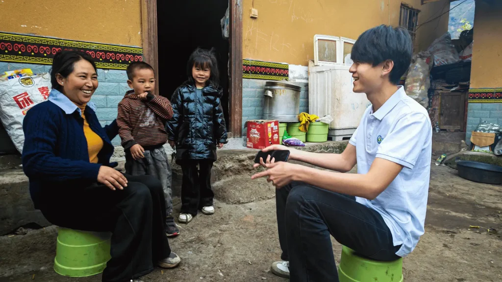 A woman sits on a stool with two children beside her, all smiling and enjoying a moment together.