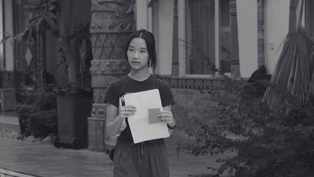 A young woman is on the sidewalk, holding a piece of paper, with a look of concentration on her face.