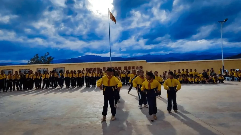 A group of students wearing yellow shirts stands in front of a flag, smiling and posing for the photo.