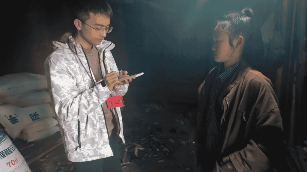 In a room, a man and woman are engaged in conversation, looking at a cell phone together.