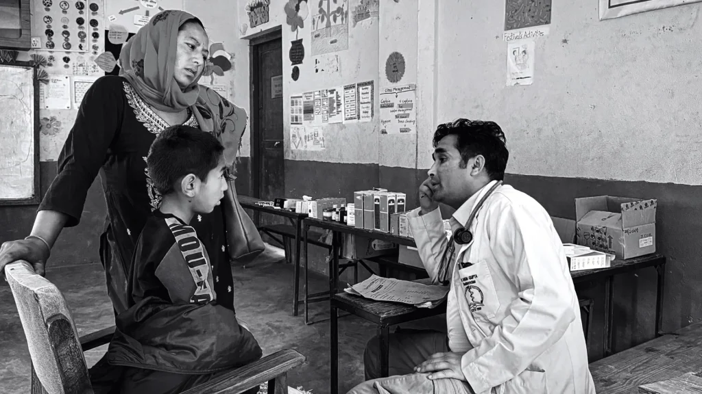 Black-and-white clinic scene: a mother and child consult a seated doctor in a white coat, creating a serious, attentive healthcare moment.